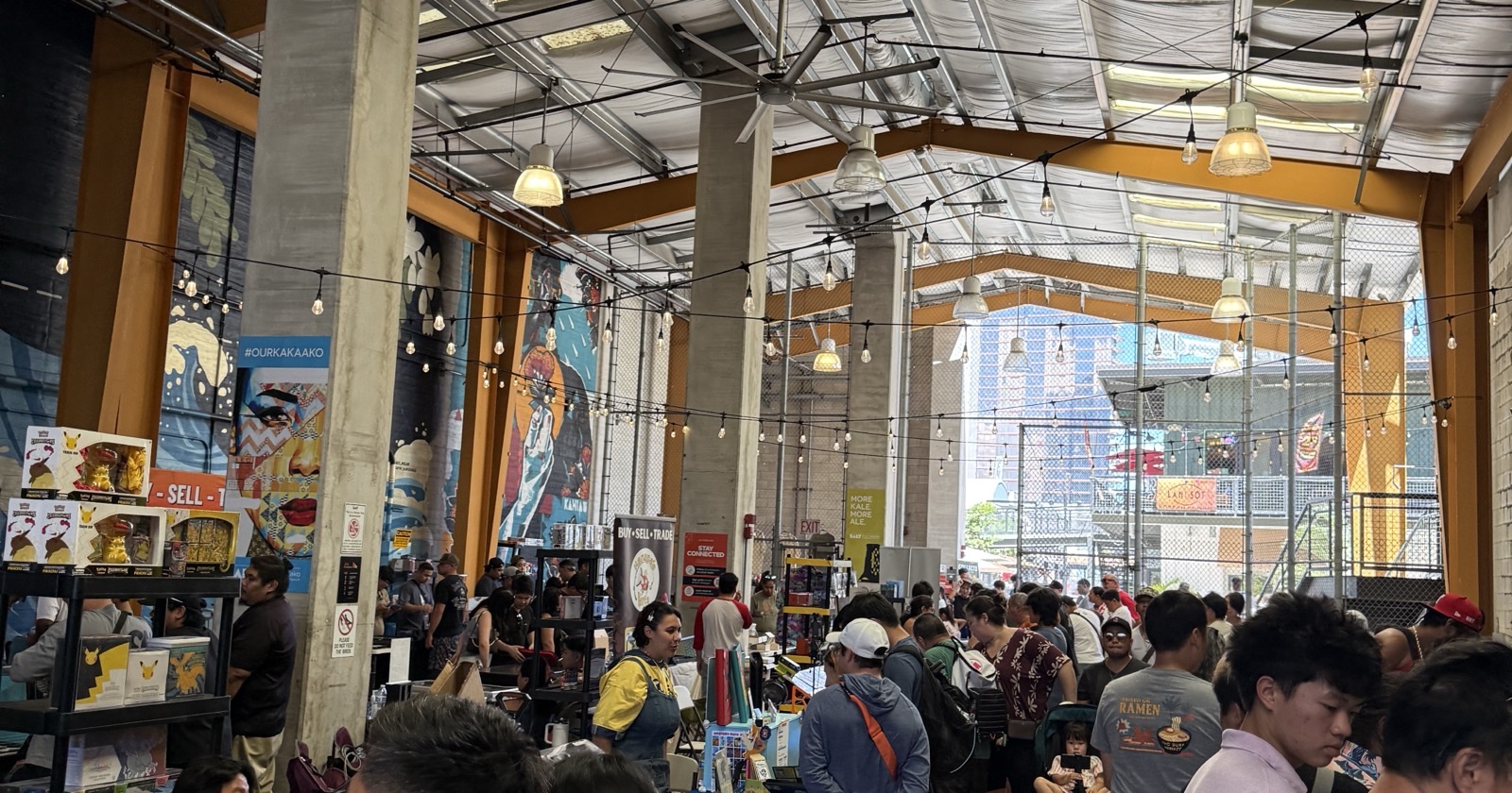 A packed Keep It Aloha Card Show floor at SALT at Our Kaka'ako — collectors, vendor tables, and Kaka'ako murals under string lights, July 2026