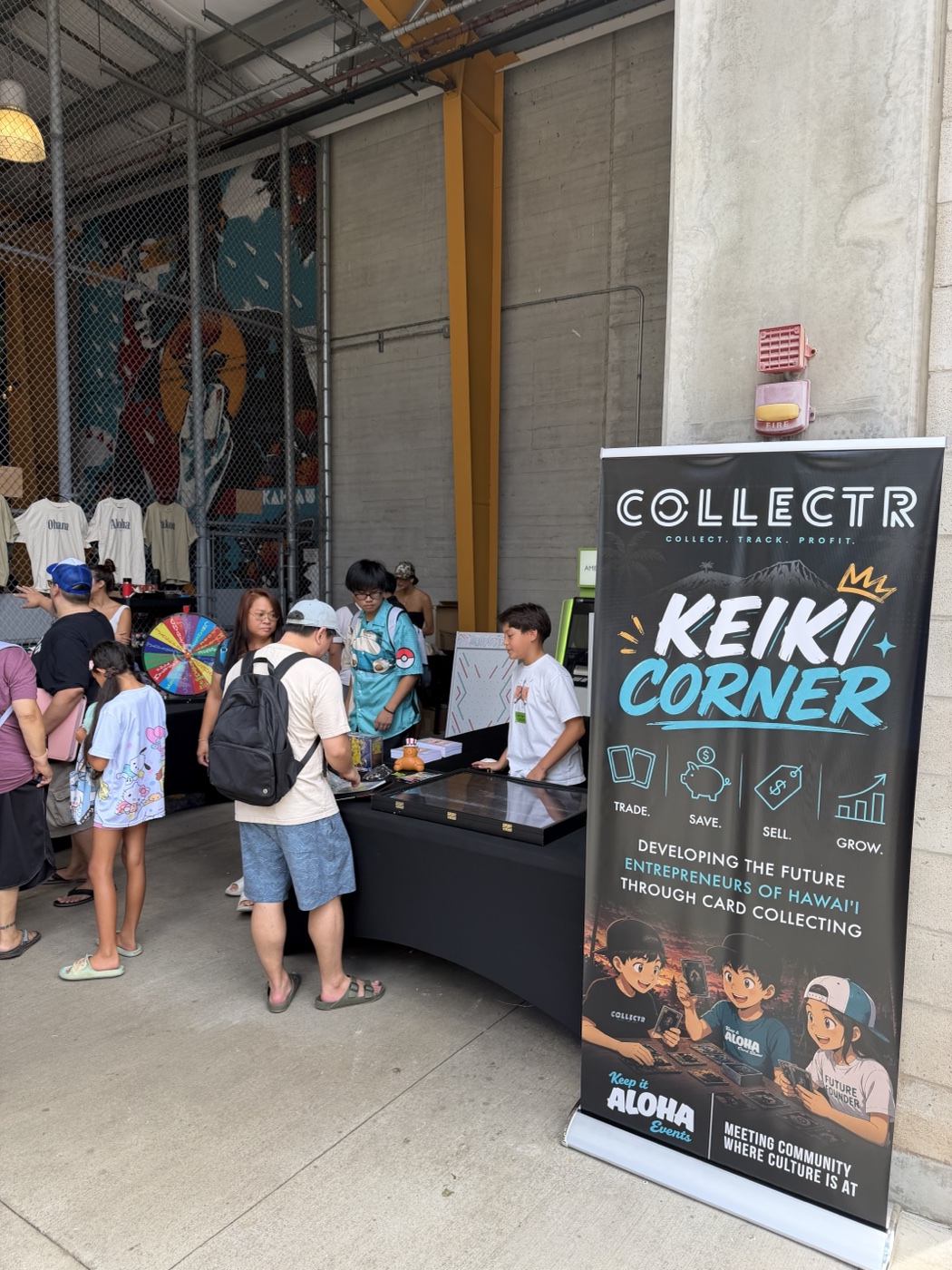 The Keiki Corner banner and table at Keep It Aloha, sponsored by Collectr, with kids gathered around